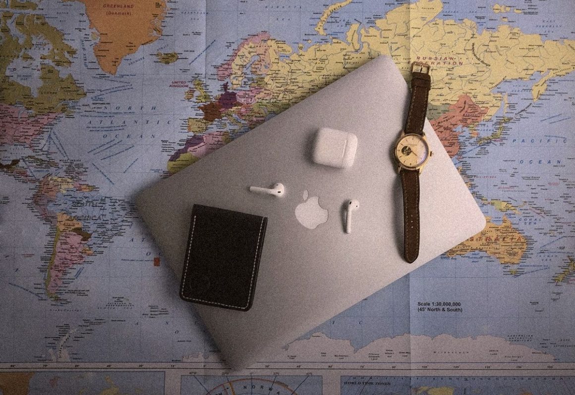 Laptop, watch and earbuds on a world map, AI travel planners vs ChatGPT