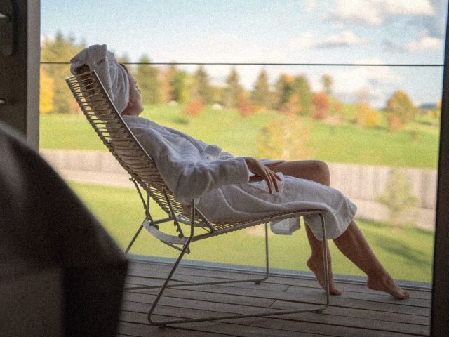 Woman in a bathrobe on a lounger facing green hills, are longevity retreats worth it