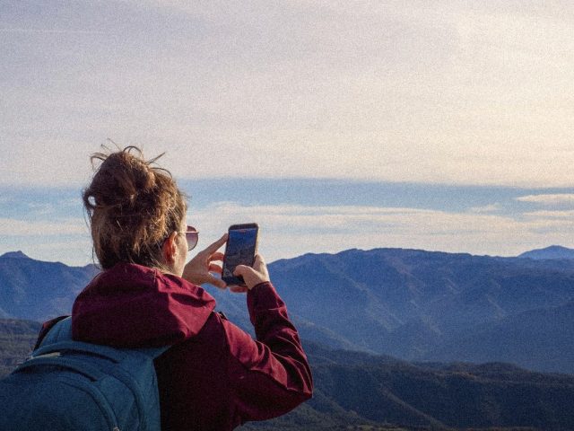 Hiker photographing a mountain view, best hiking apps