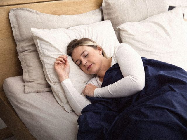 Woman asleep under a navy blanket, best sleep earbuds