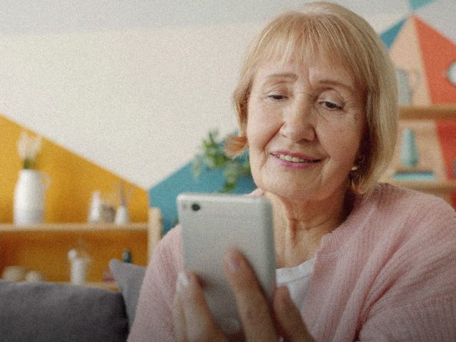 Older woman smiling at her phone at home, companion robots for elderly people