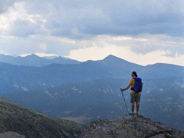 Hiker with a blue backpack on a mountain summit, Garmin inReach review