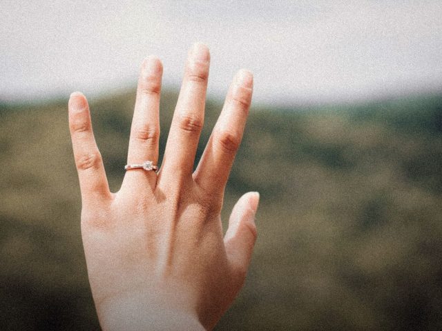 Hand wearing a ring against a soft green background, RingConn review