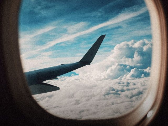 Aircraft wing seen through a cabin window above clouds, Travel Guard review