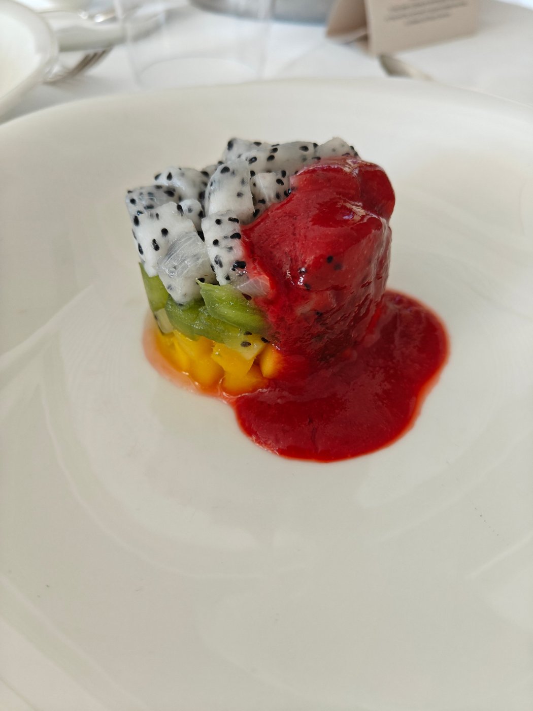 A small tower of mango, kiwi and dragon fruit with a red berry coulis