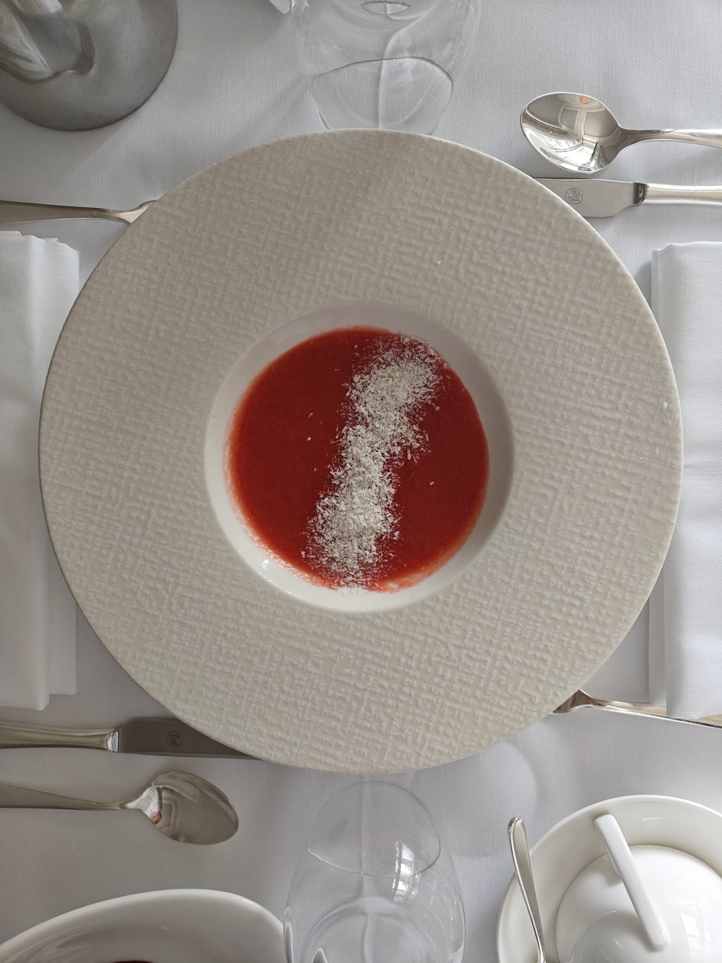A small bowl of red vegetable soup with a sprinkle on top, served in a wide plate