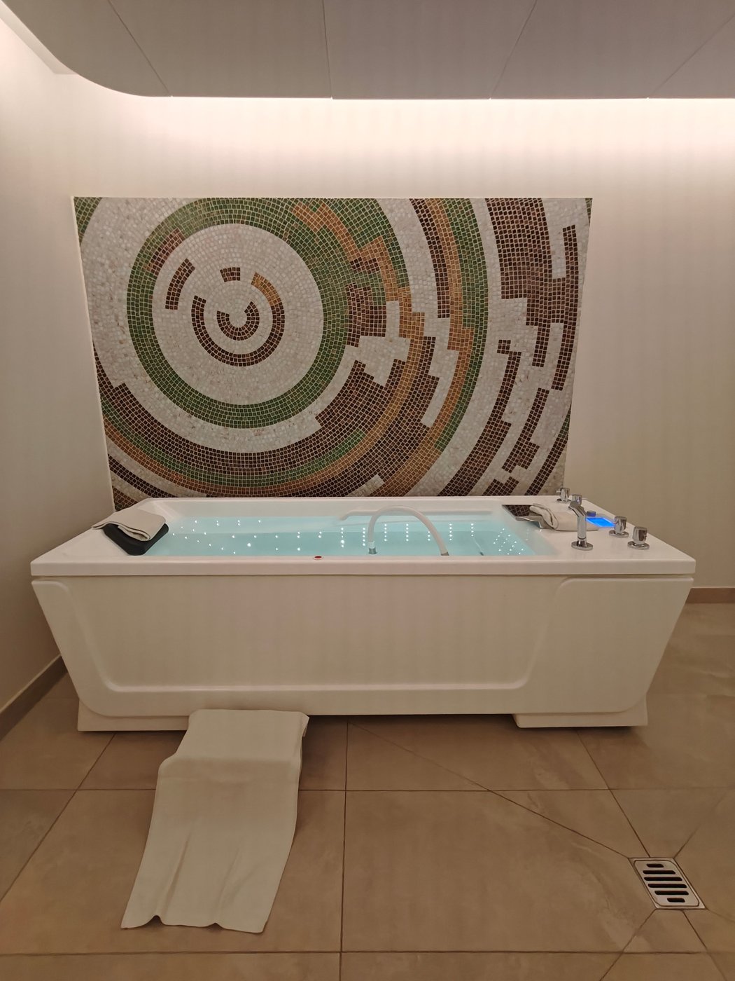 A hydrotherapy tub with underwater jets and lights in front of a mosaic wall