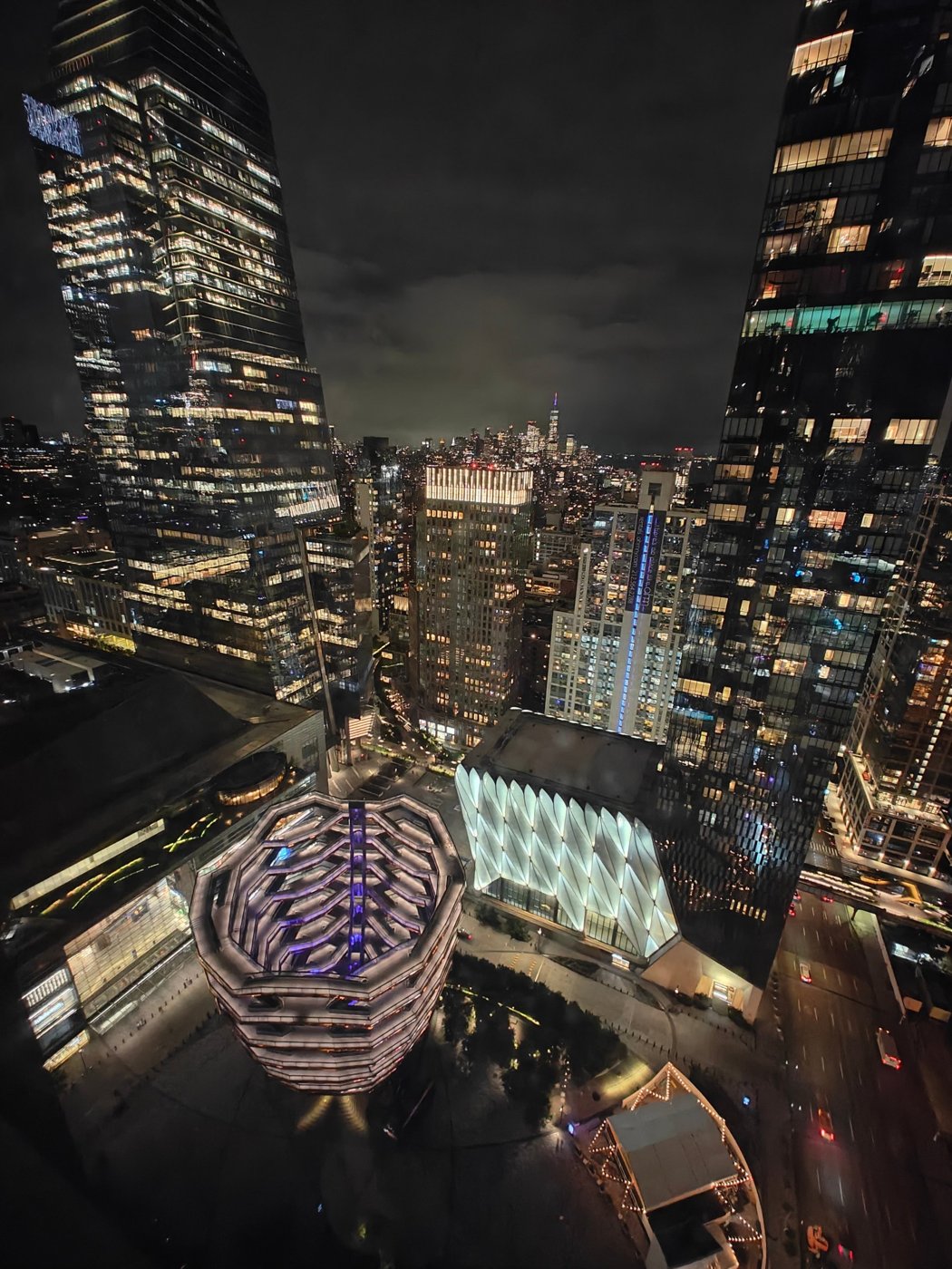 Night view looking down onto the Vessel and The Shed in Hudson Yards, with Midtown and Lower Manhattan lit up beyond